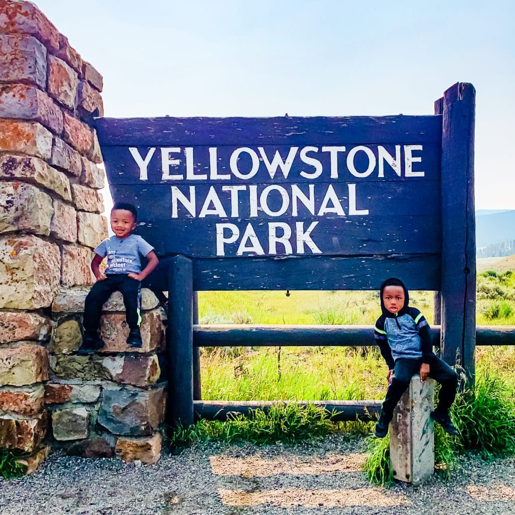Twin boys posing with the Yellowstone National Park sign during their Bozeman to Yellowstone road trip.