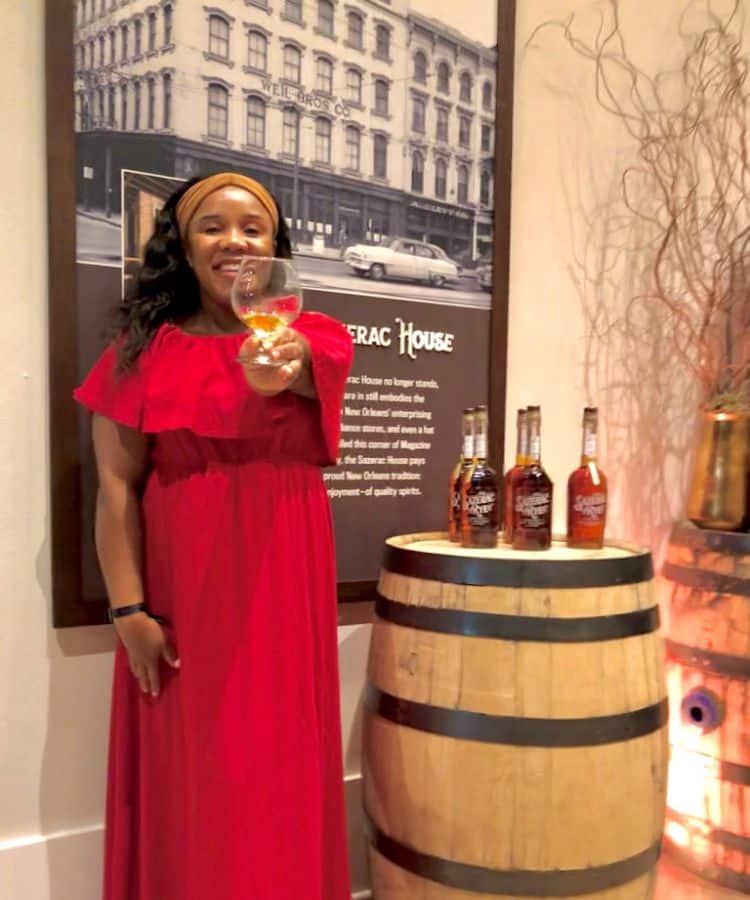 Holding a shot of the Sazerac House's famous rye whiskey, in front of a barrel and bottles of their signature spirit. Such a fun thing to do in New Orleans.