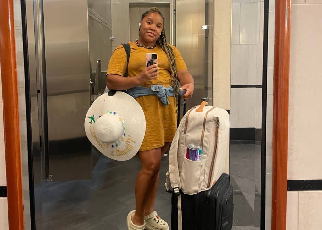 Me taking a selfie in the airport bathroom with my carry on, travel backpack, and straw hat. 