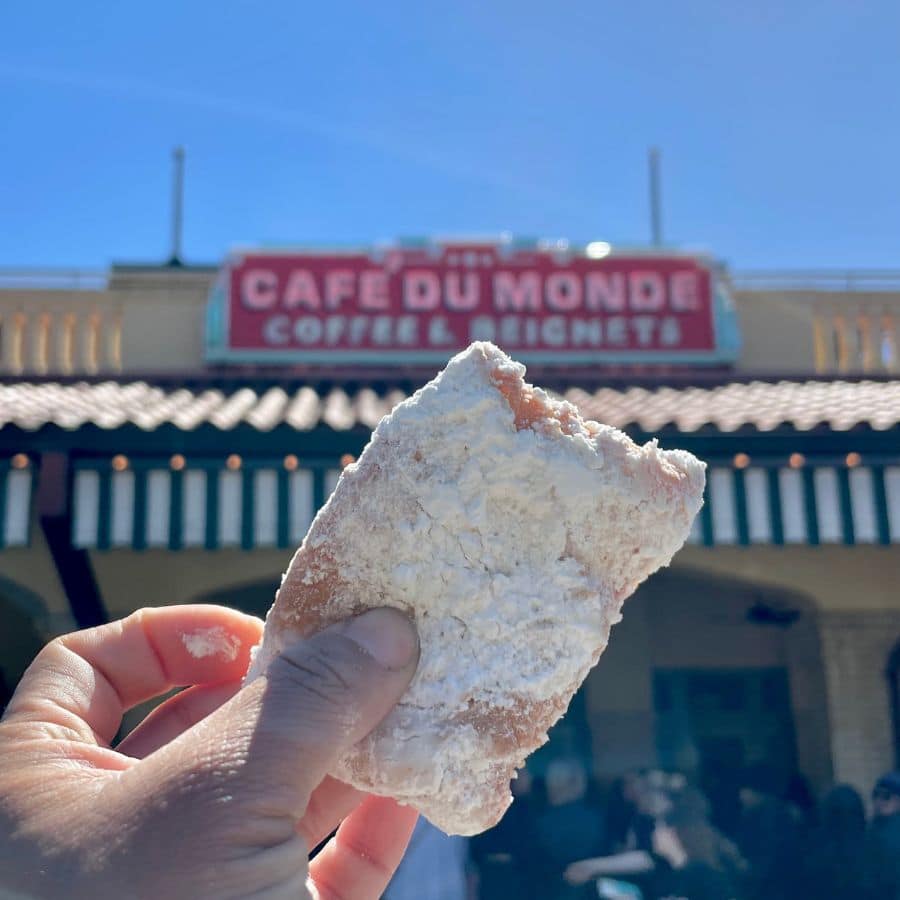 holding a freshly made beignet in front of Cafe Du Monde- a must-visit in New Orleans