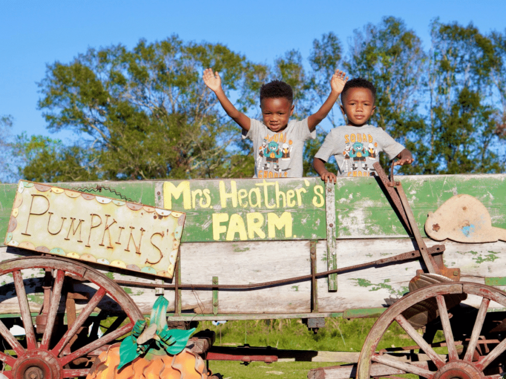 The boys in a green wagon with the sign "Mrs. Heather's Farm" and "pumpkins" during fall in New Orleans.